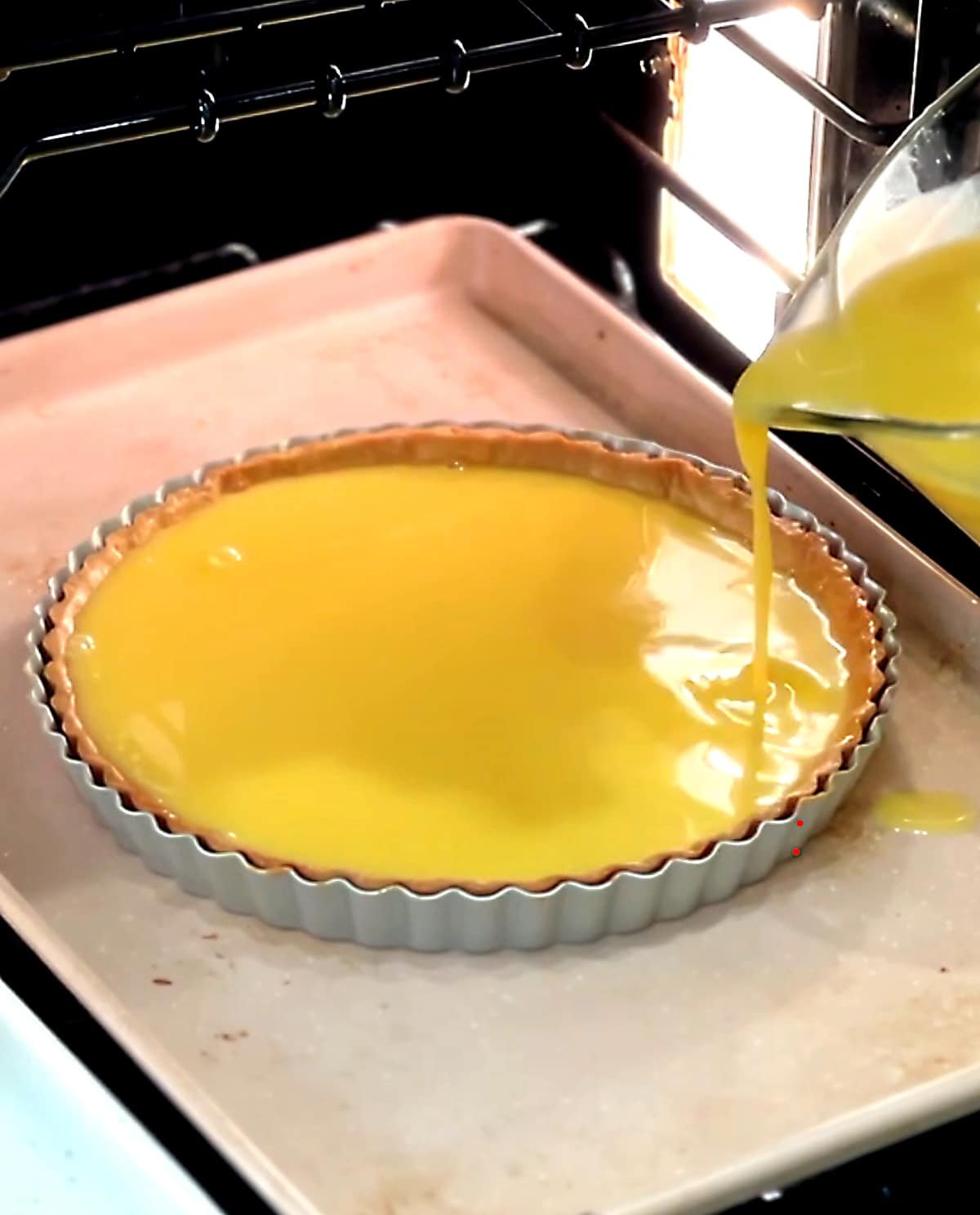 pouring lemon filling into blind baked tart shell in the oven