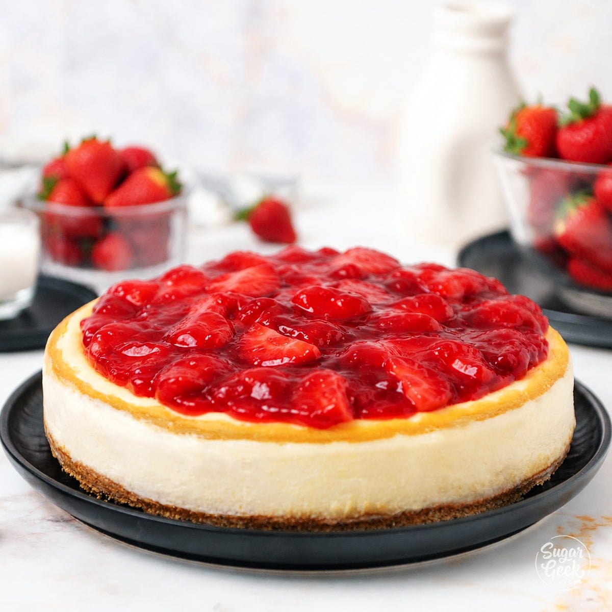 Strawberry cheesecake on a black plate with strawberries in the background.
