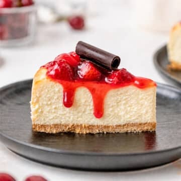 Slice of strawberry cheesecake with a chocolate curl on top on a black plate.