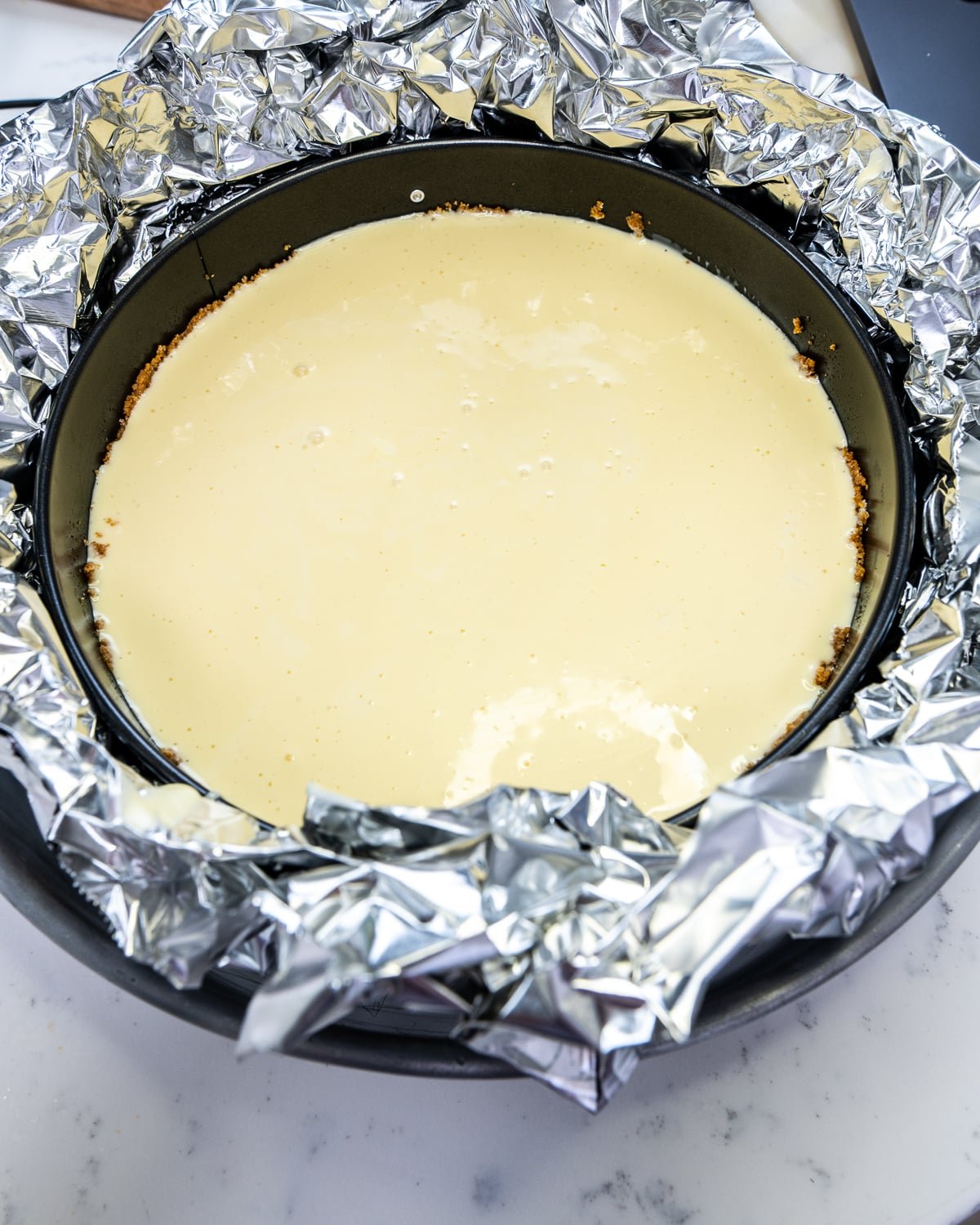 closeup of prepared cheesecake in a pan with tinfoil