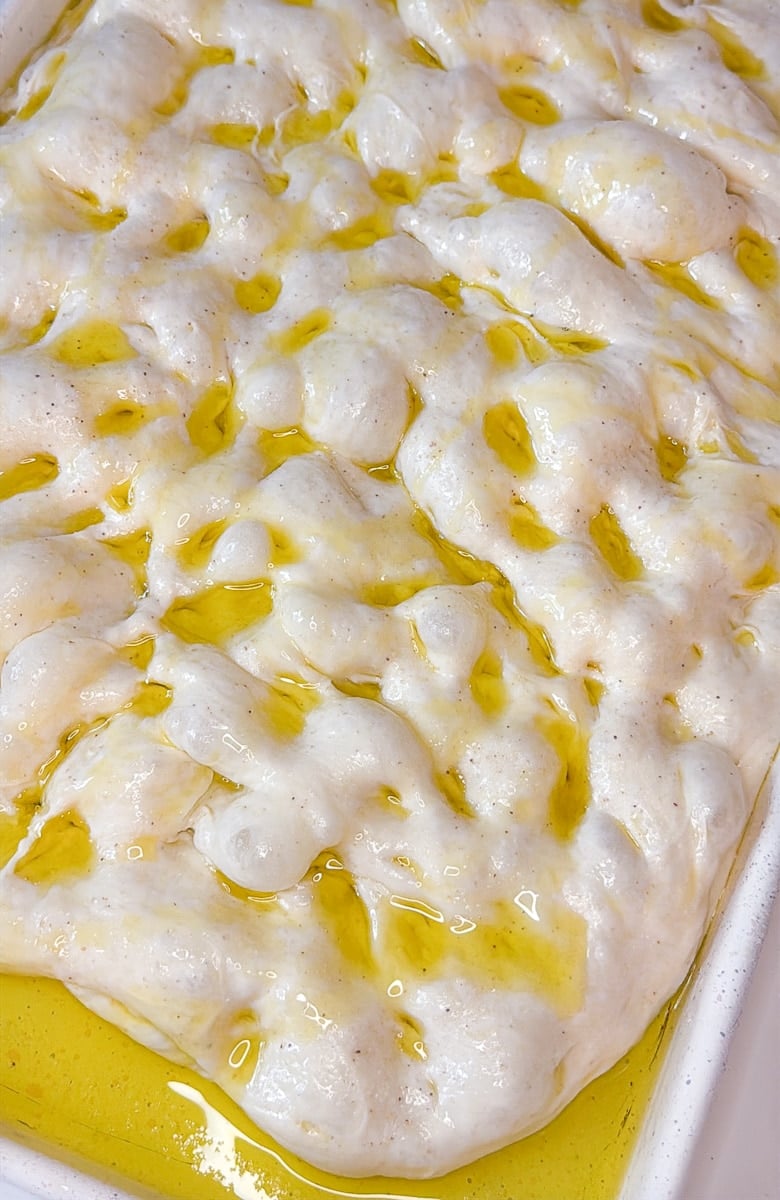 Sourdough focaccia on a sheet pan dimpled with olive oil.