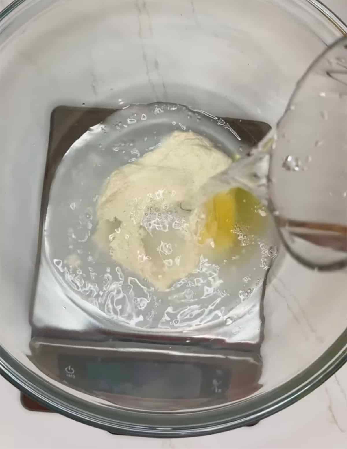 Dissolving water, sourdough starter, and honey in a clear glass bowl.