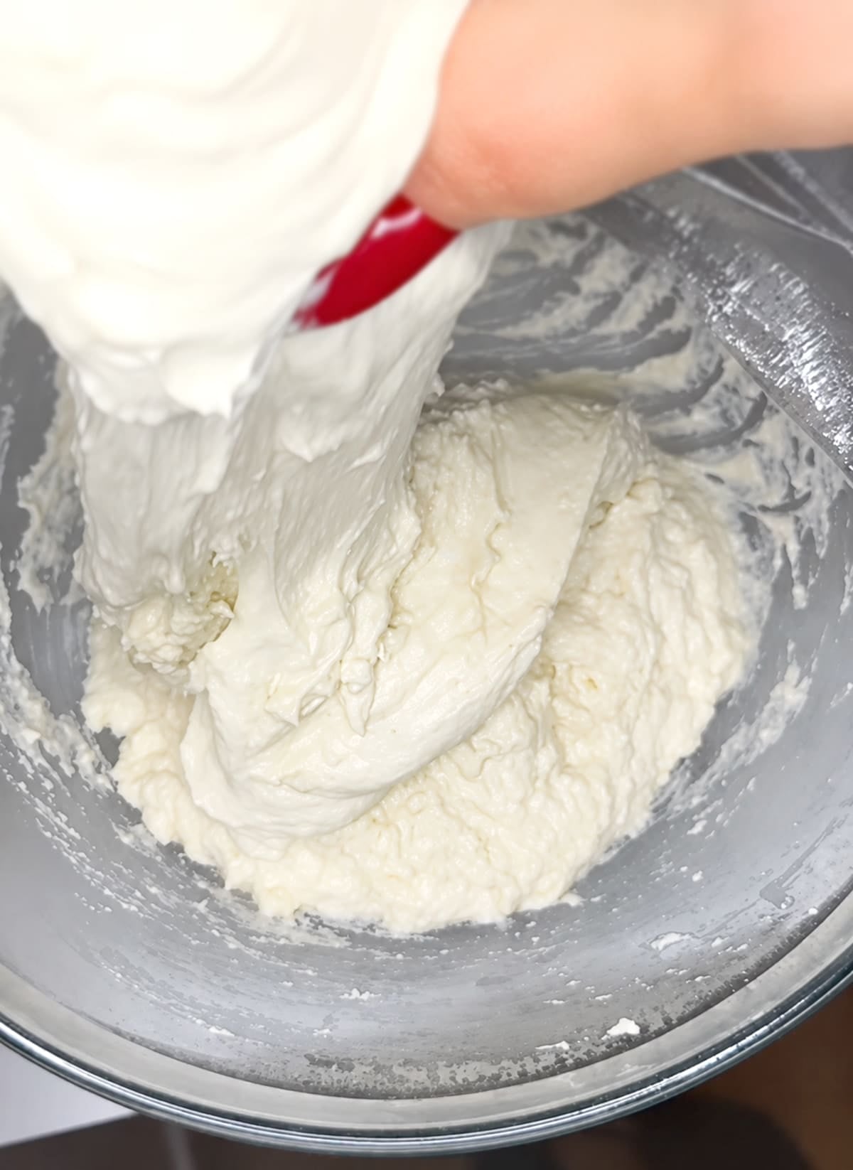 Hand pulling and stretching sourdough focaccia dough out of a clear glass bowl.