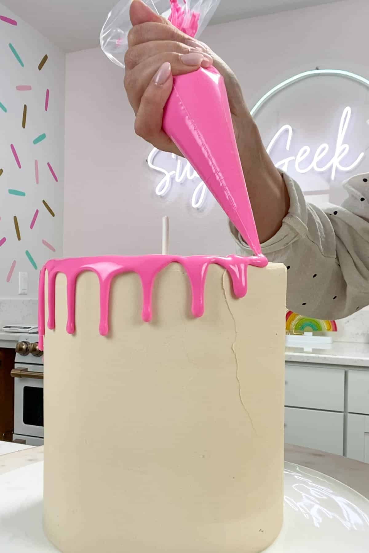 Pink piping bag piping drips on top of a white cake.