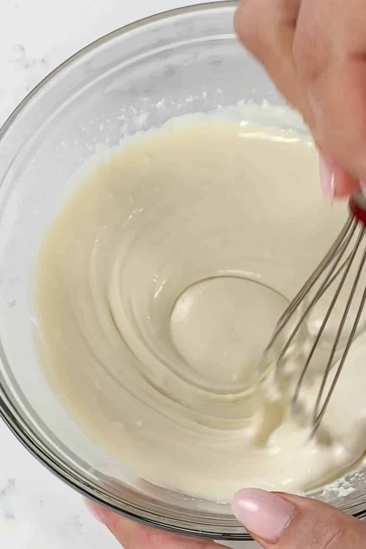 Whisk mixing white chocolate mixture in a clear bowl.