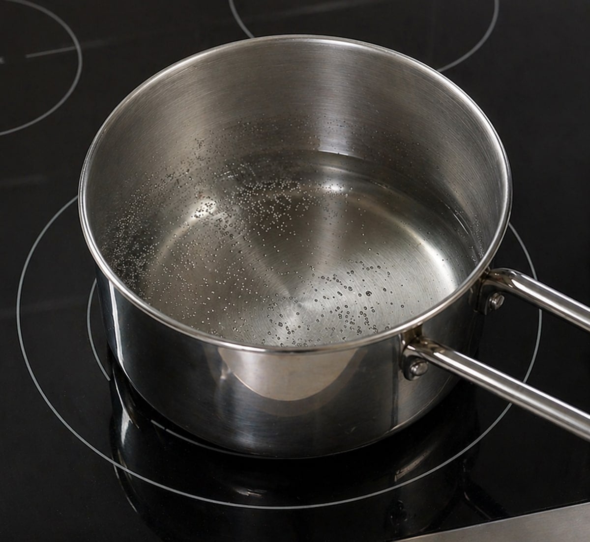 Saucepan with water inside on a black stovetop.