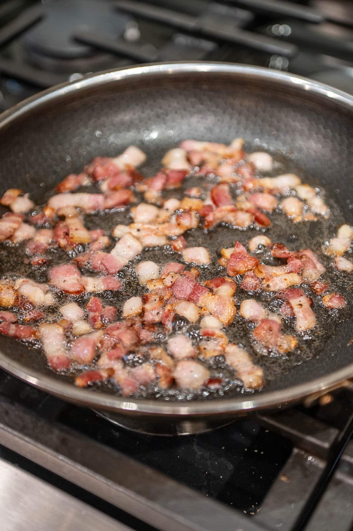 Small pieces of bacon cooking in a got skillet. 