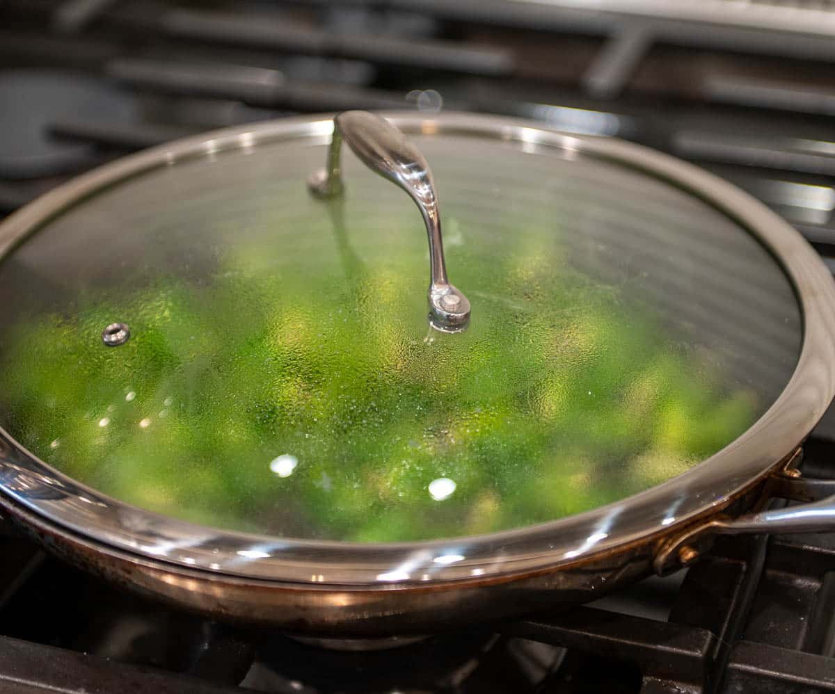 The skillet's lid is placed on the skillet to create moisture and cook the Brussel sprouts fully.