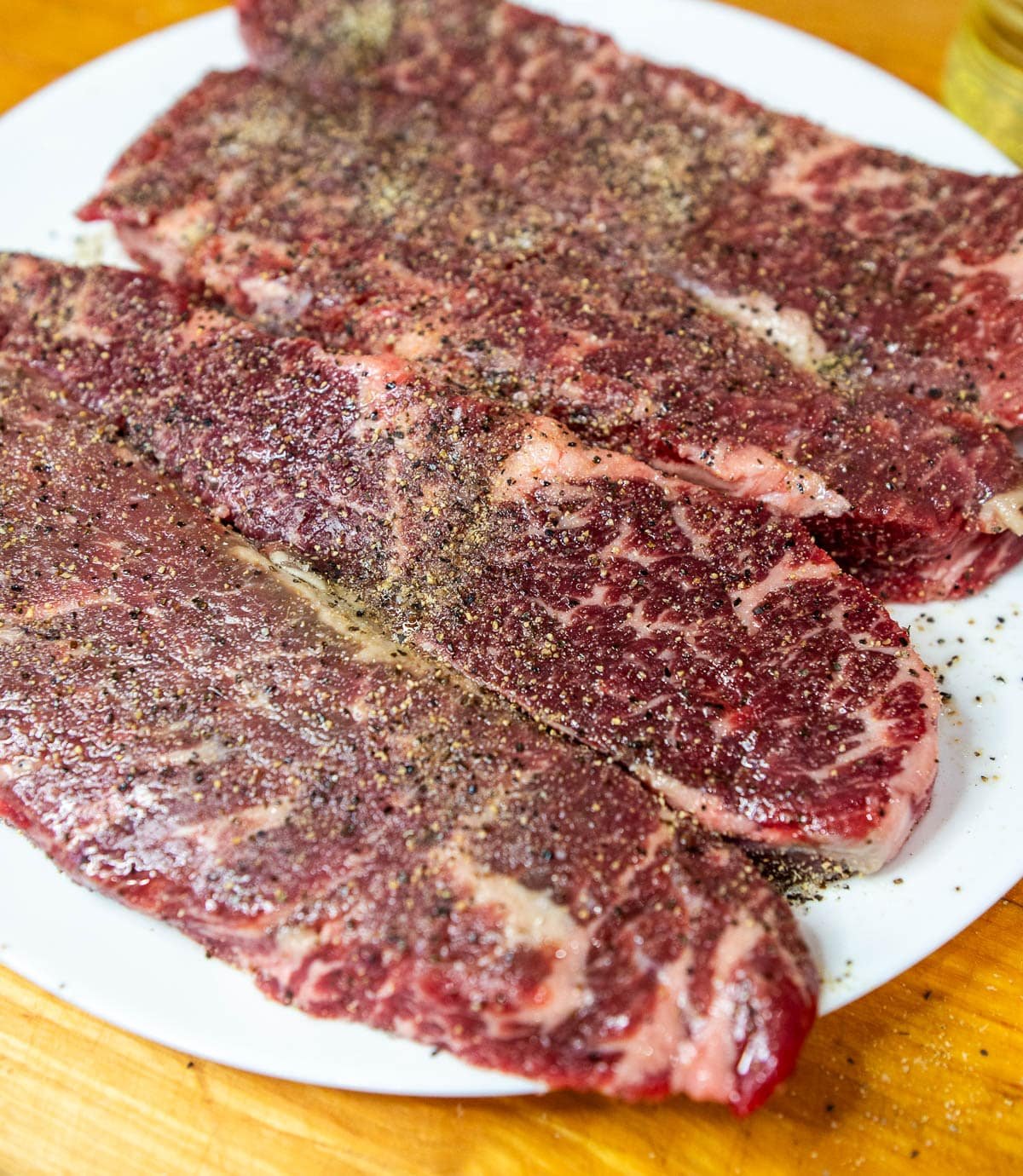Raw, boneless beef short ribs seasoned on a plate.