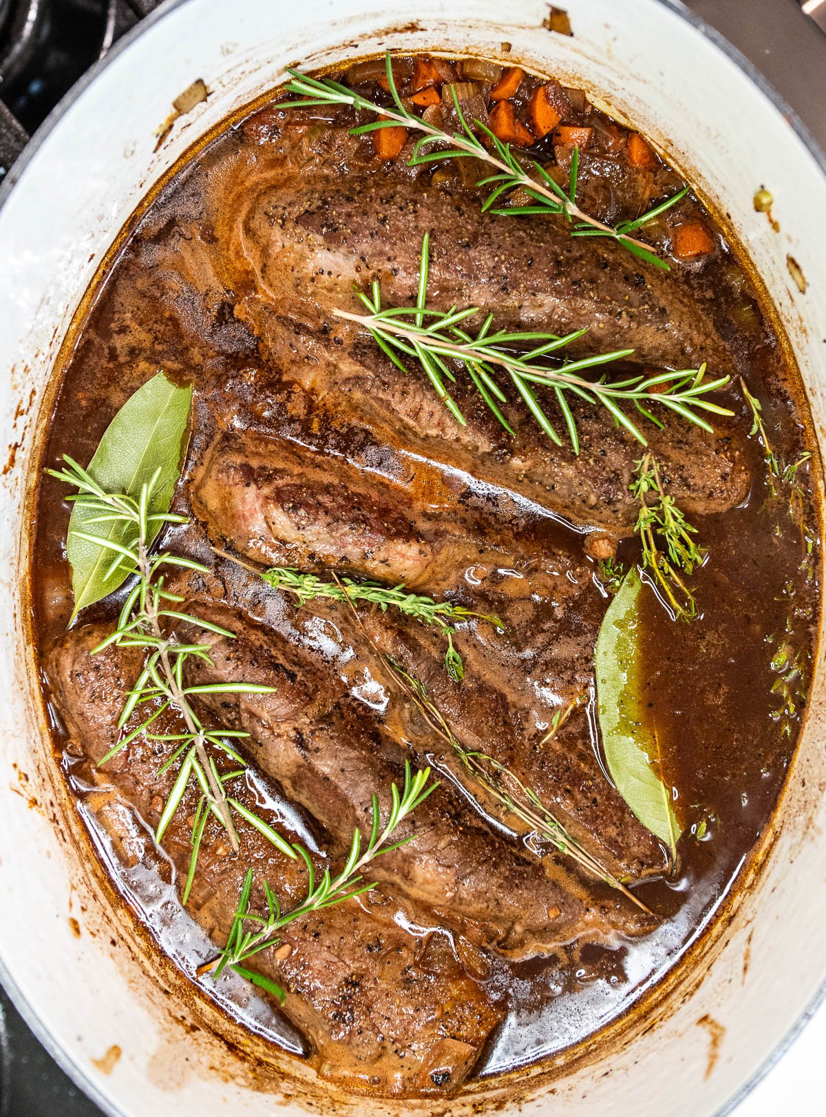 Beef short ribs added back into the dutch oven with beef broth, wine, and herbs.