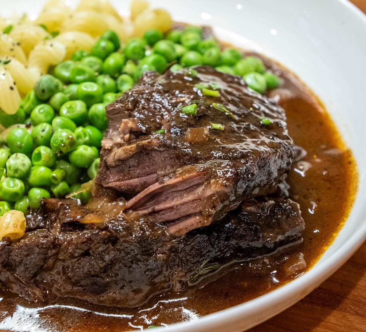 close up of beef short ribs on a plate with peas and mashed potatoes