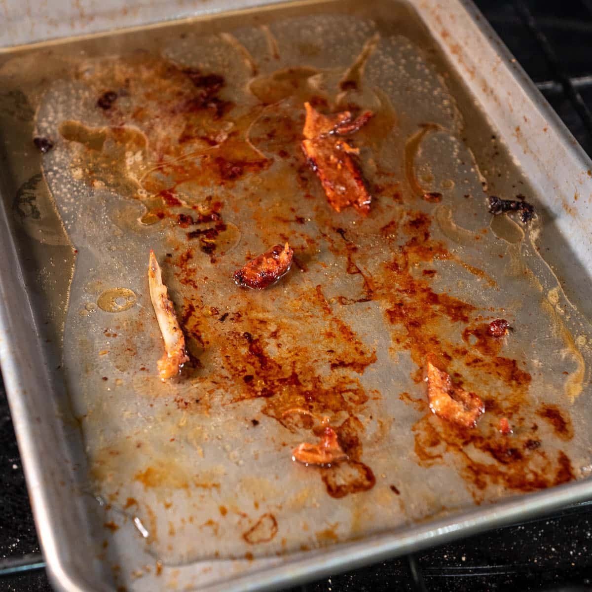 The remnants from the roasted chicken spine making chicken drippings on a baking sheet.