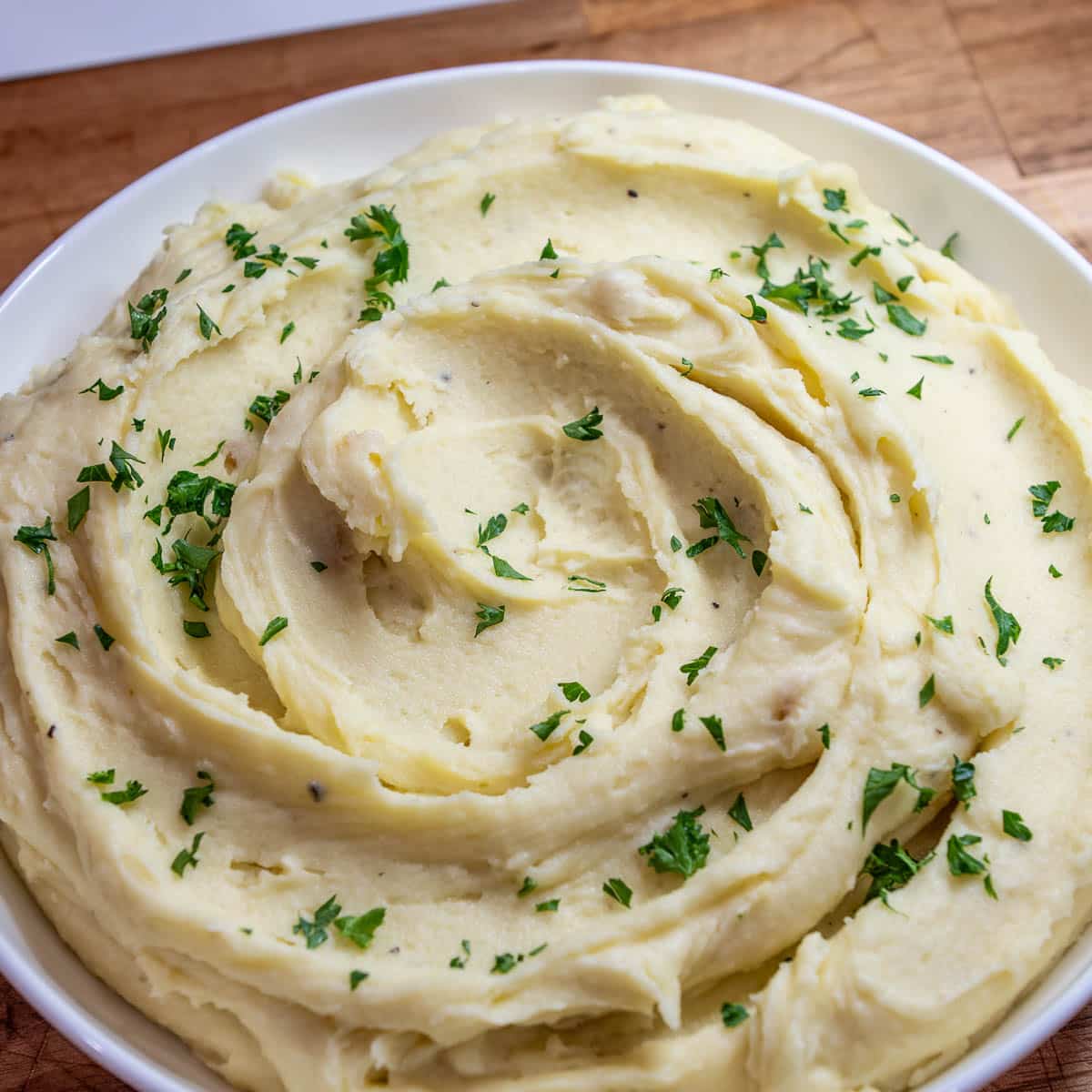 A bowl of creamy mashed potatoes garnished with freshly chopped parsley.
