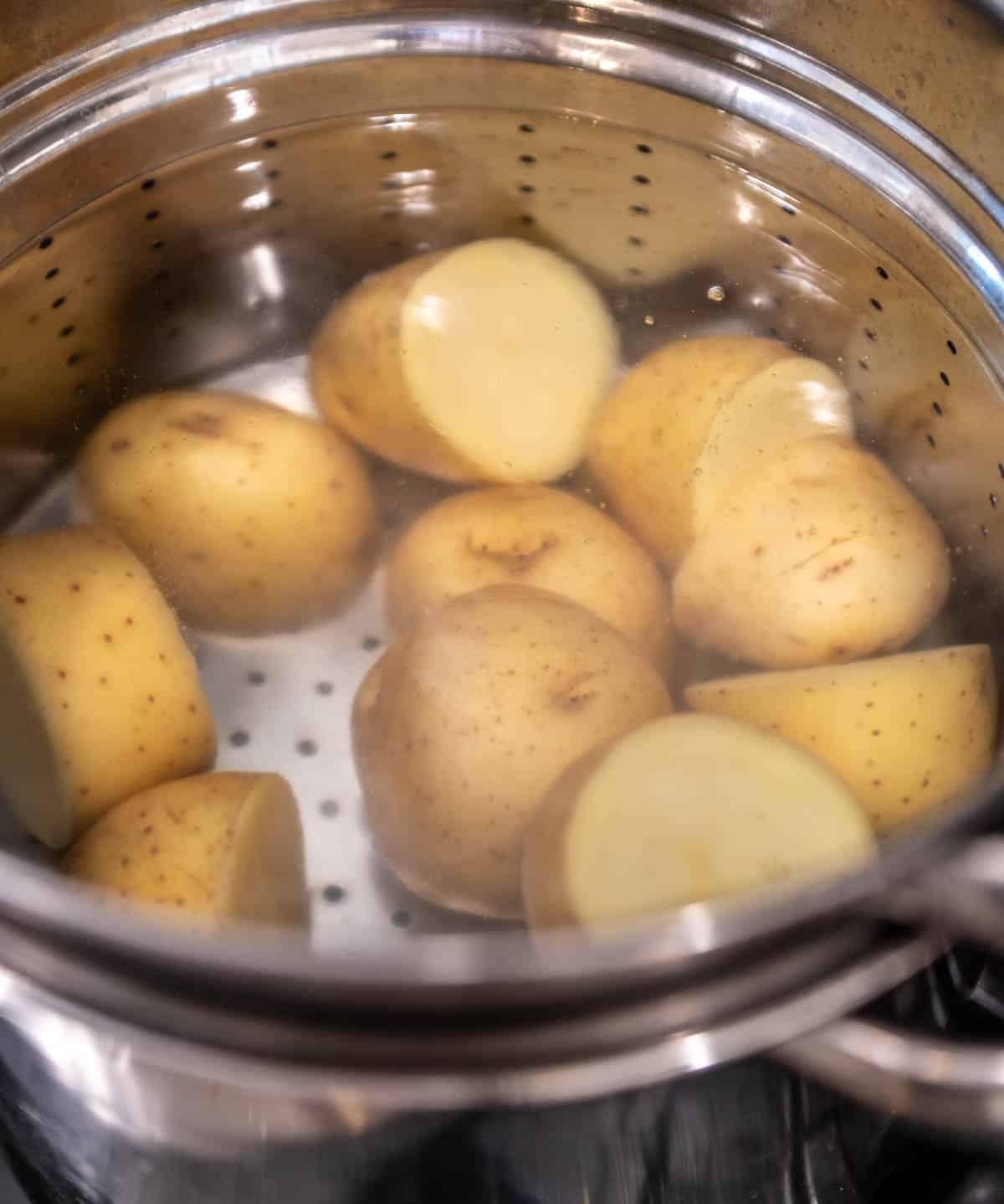 A large pot with water and potatoes sliced in half.