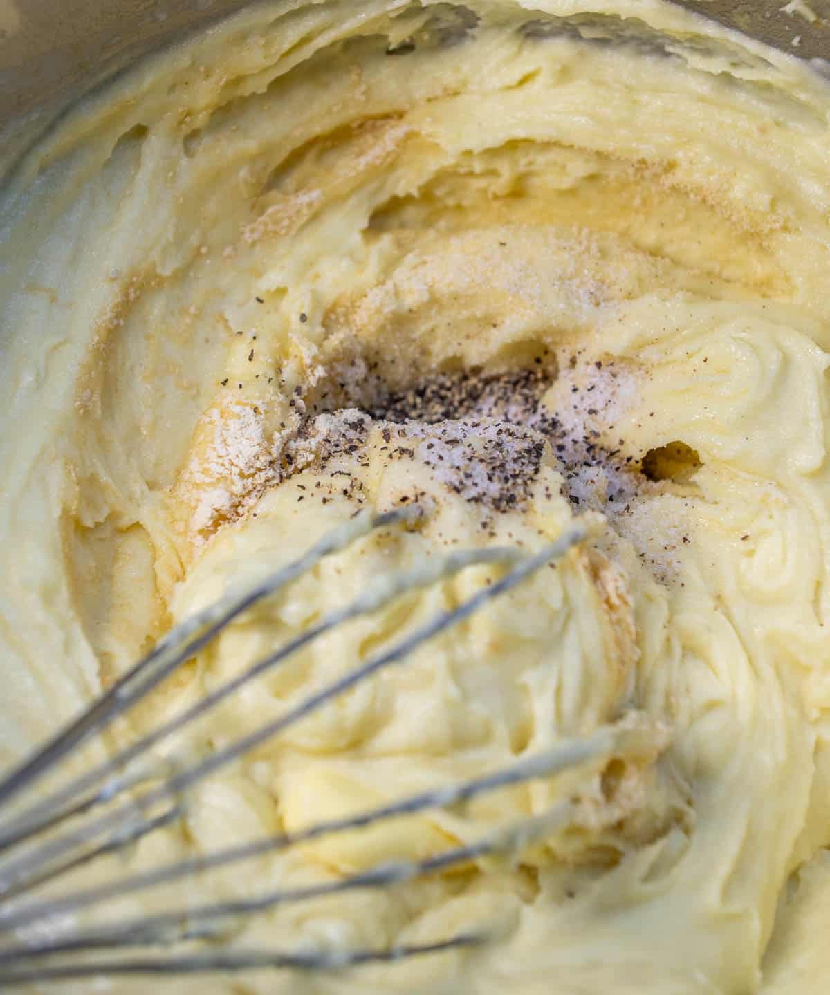 Creamy mashed potatoes with seasoning and heavy cream, mixed together with a whisk.
