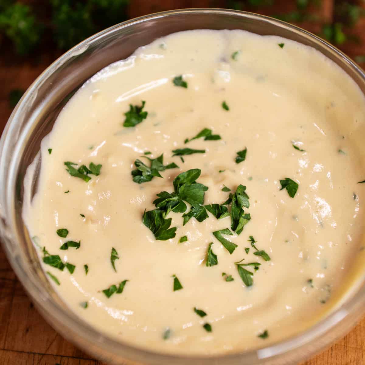 Creamy Dijon sauce in a glass bowl, garnished with freshly chopped parley.