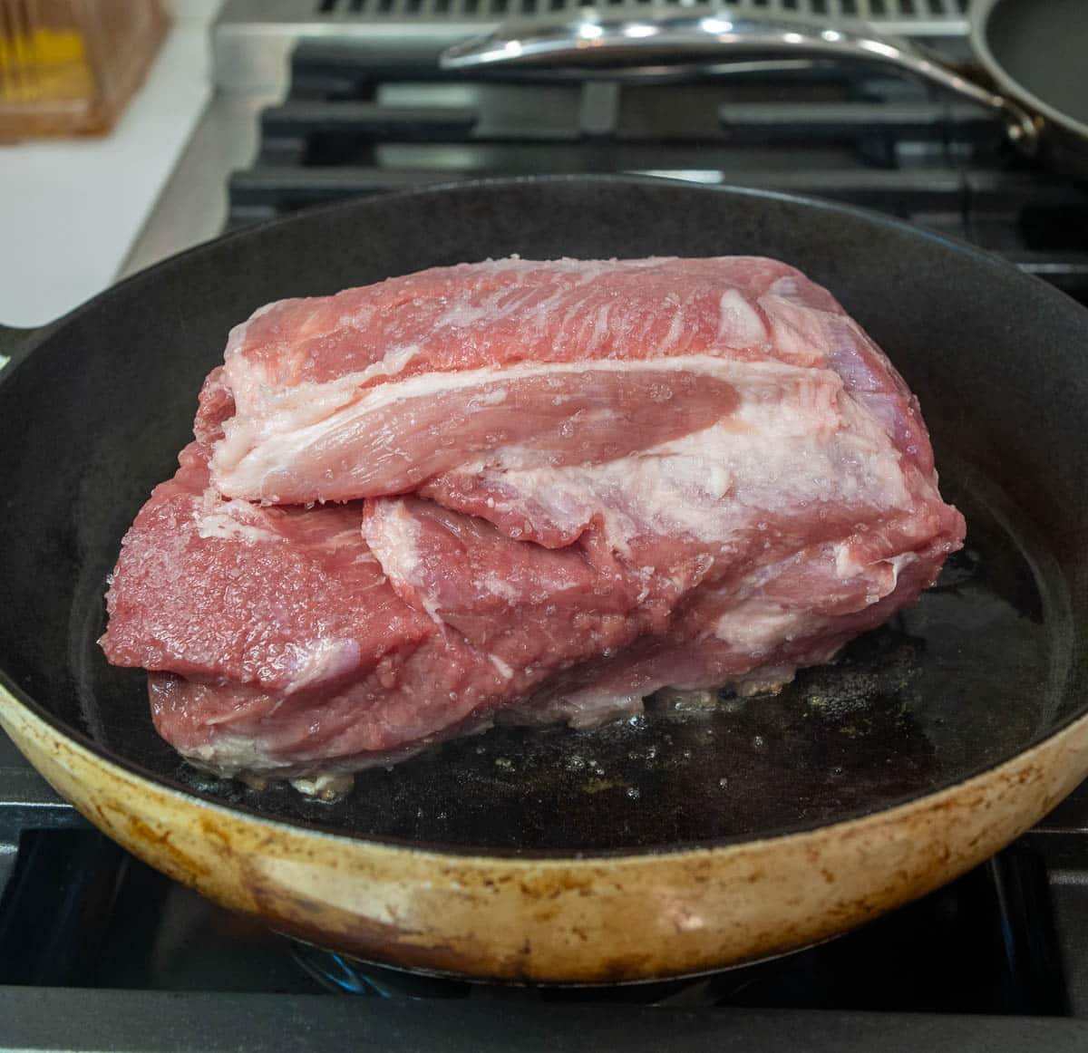 Raw pork shoulder being seared in the pan.