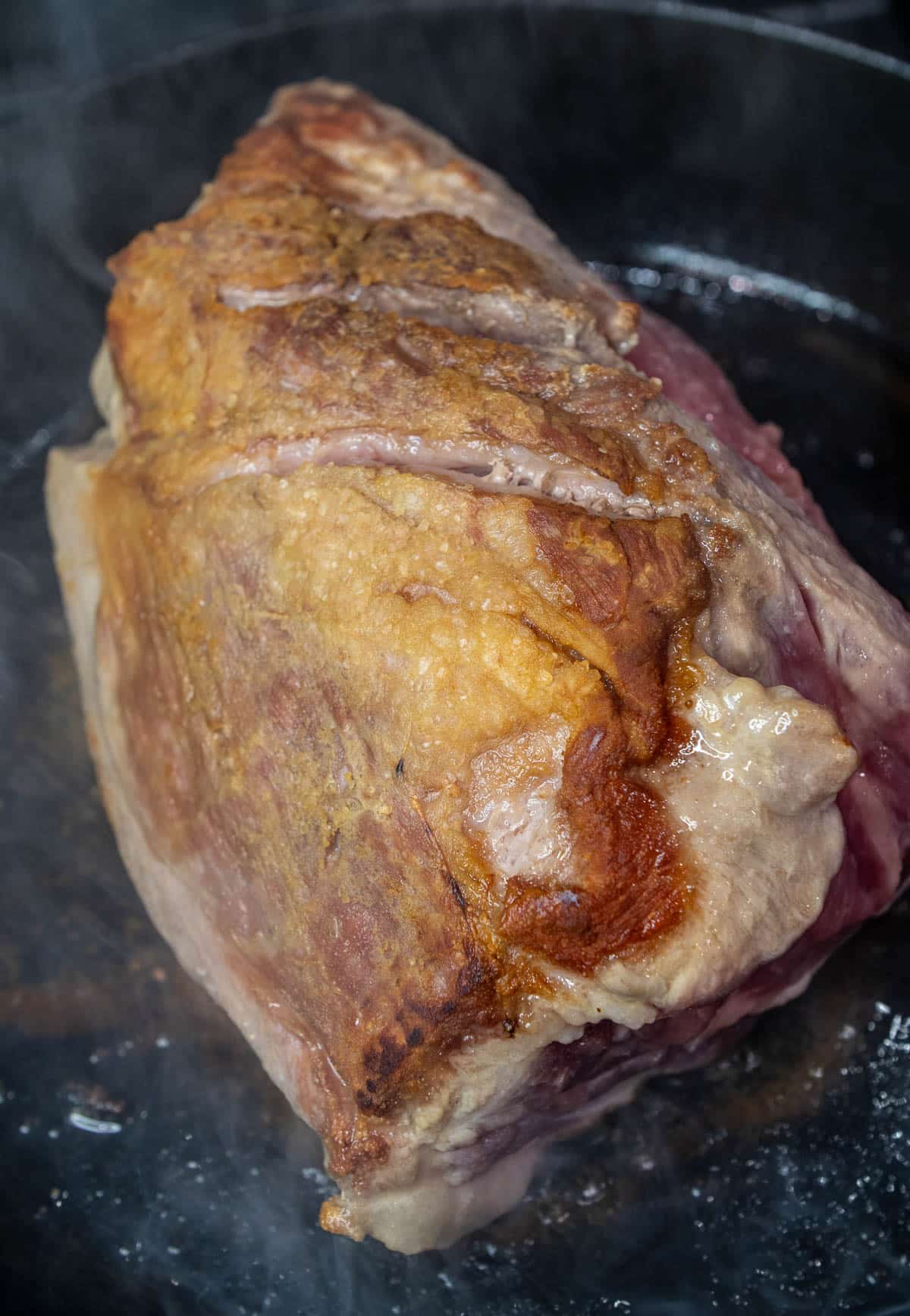 Pork shoulder roast seared to golden brown in a hot pan.