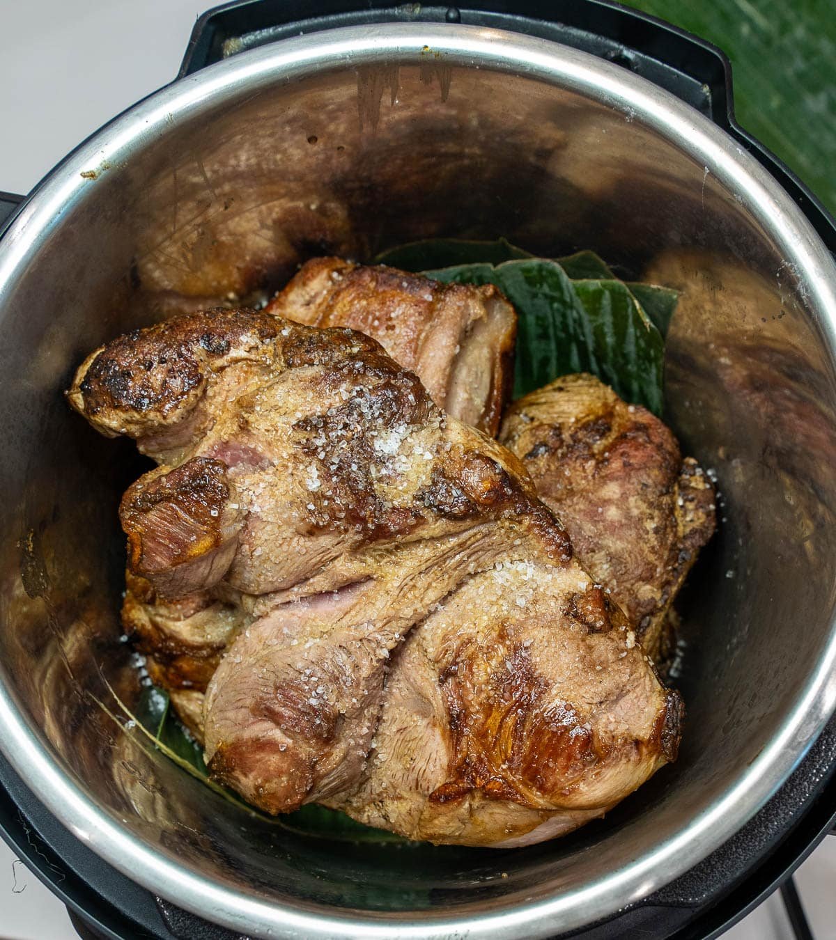 Instant pot with pork placed on top of the banana leaf and topped with salt. 