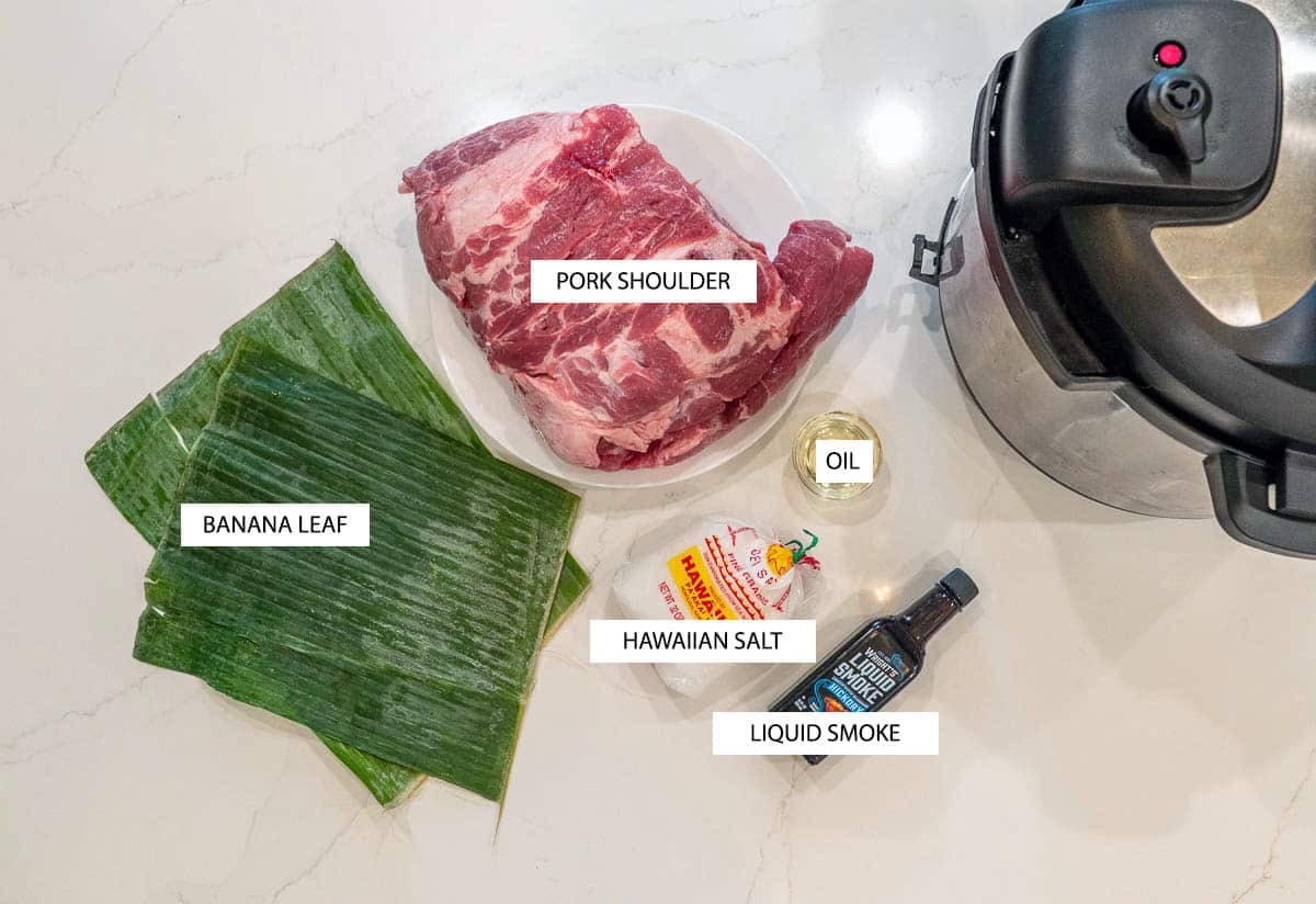 Kalua Pork recipe ingredients, featuring: a raw, whole pork shoulder, two banana leafs, Hawaiian salt, oil, liquid smoke, and an Instant Pot.