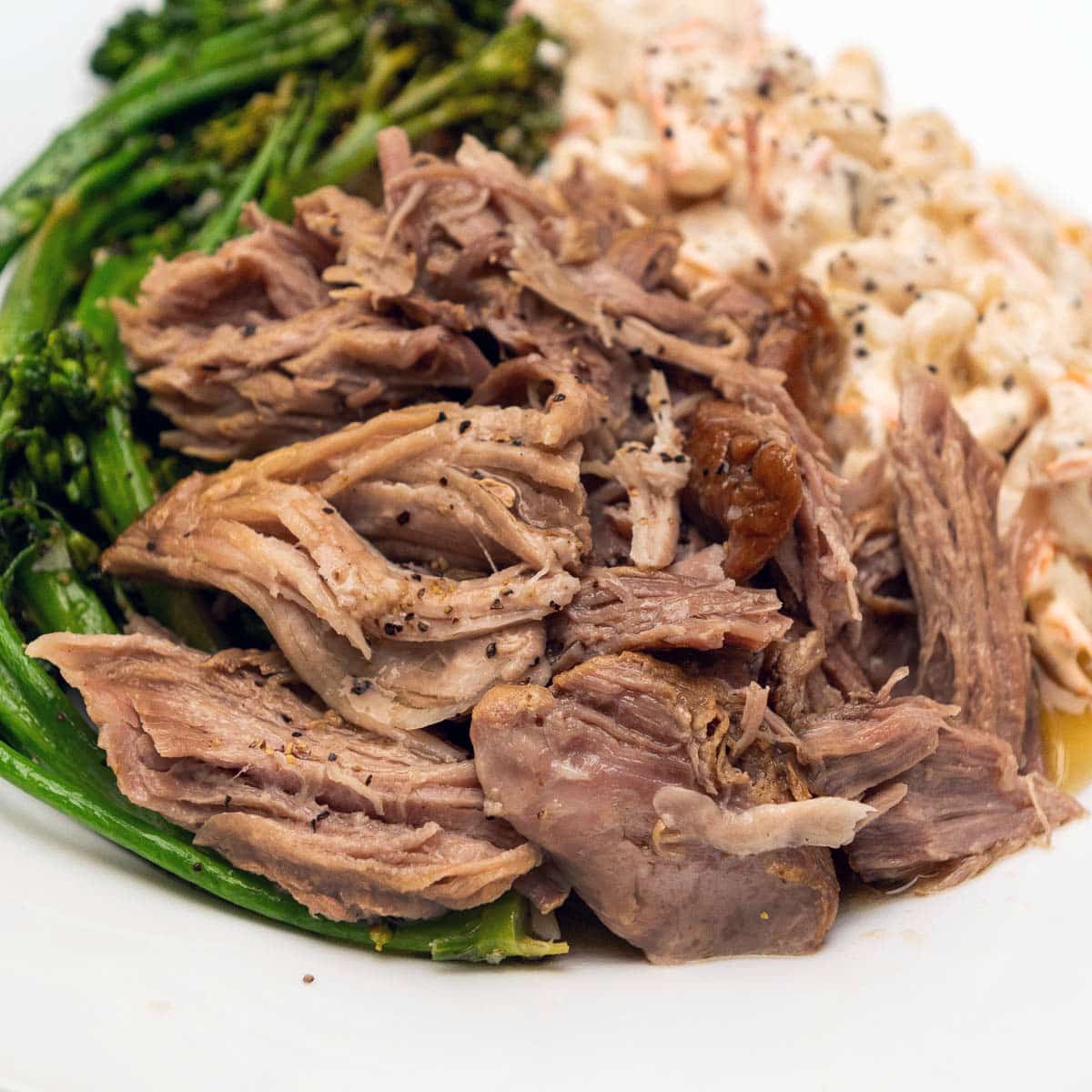 Shredded Kalua Pork on a plate with a side of broccolini and Hawaiian Mac Salad.