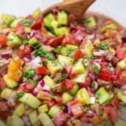 close up of Moroccan Cucumber Tomato Onion Salad in a bowl with a wooden spoon