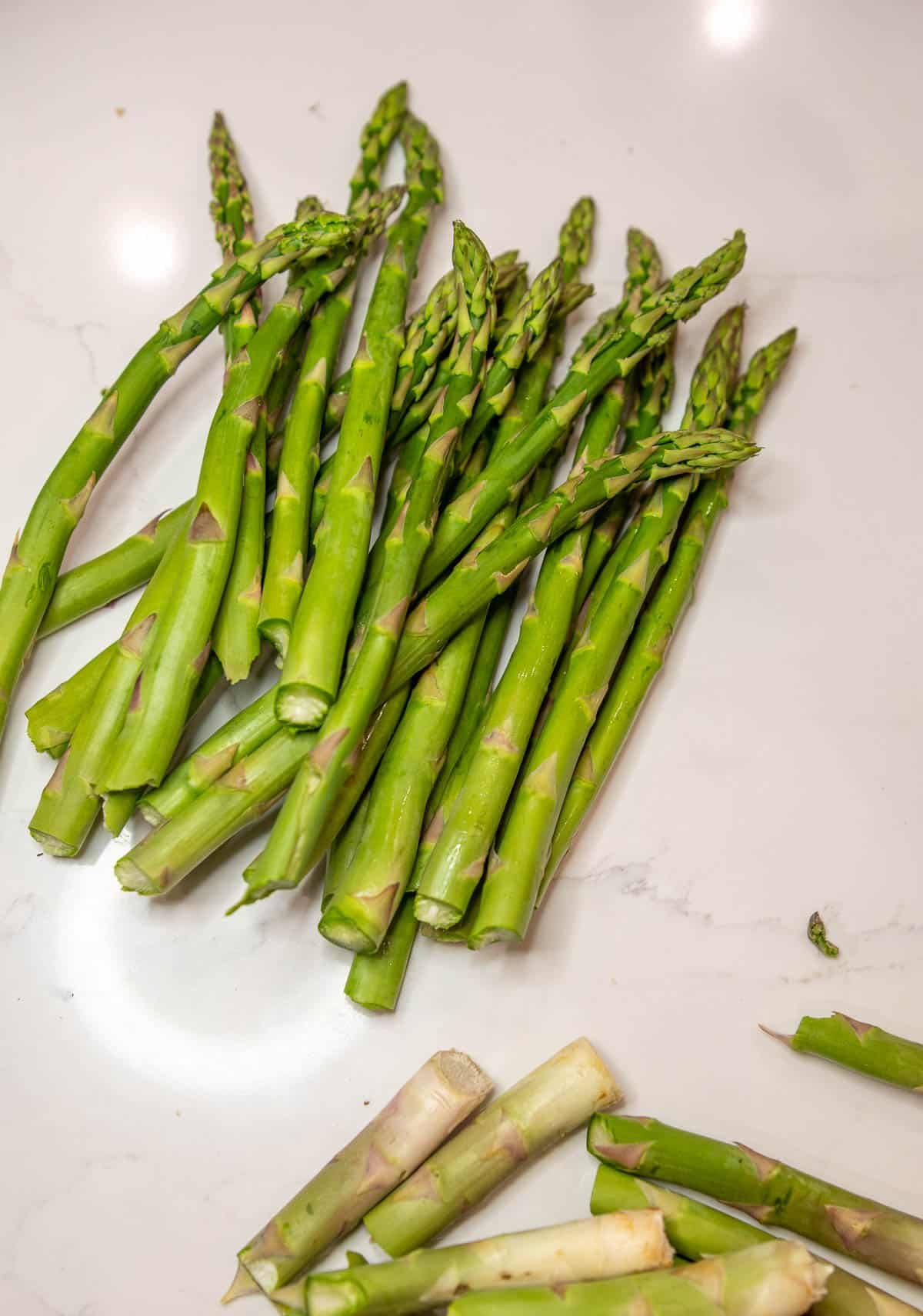 Raw asparagus with ends cut off on a marble countertop.