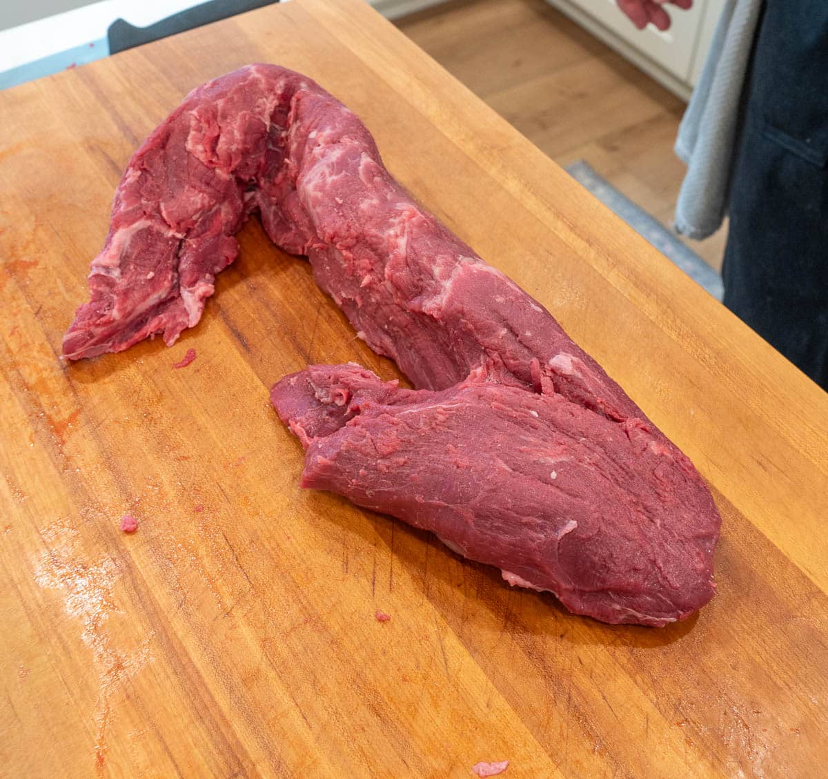 A whole, raw beef tenderloin spread apart from each end on a wood cutting board.