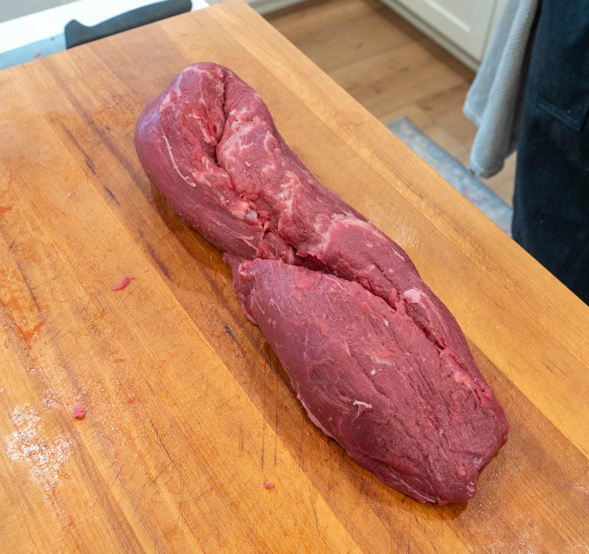A whole, raw beef tenderloin with each side folded in together on a wood cutting board.