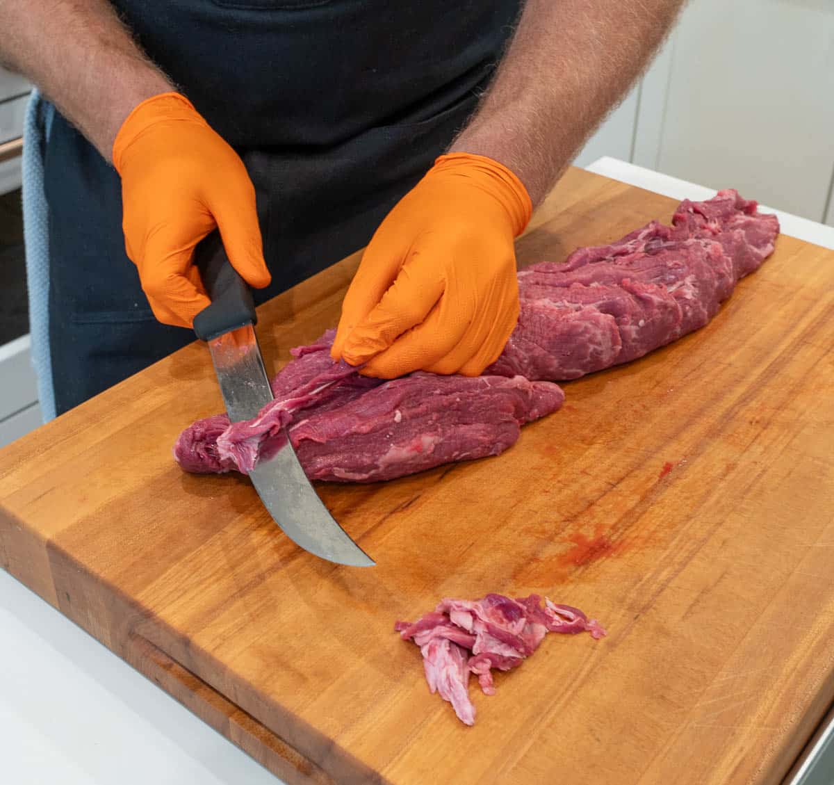 A whole, raw beef tenderloin being trimmed.