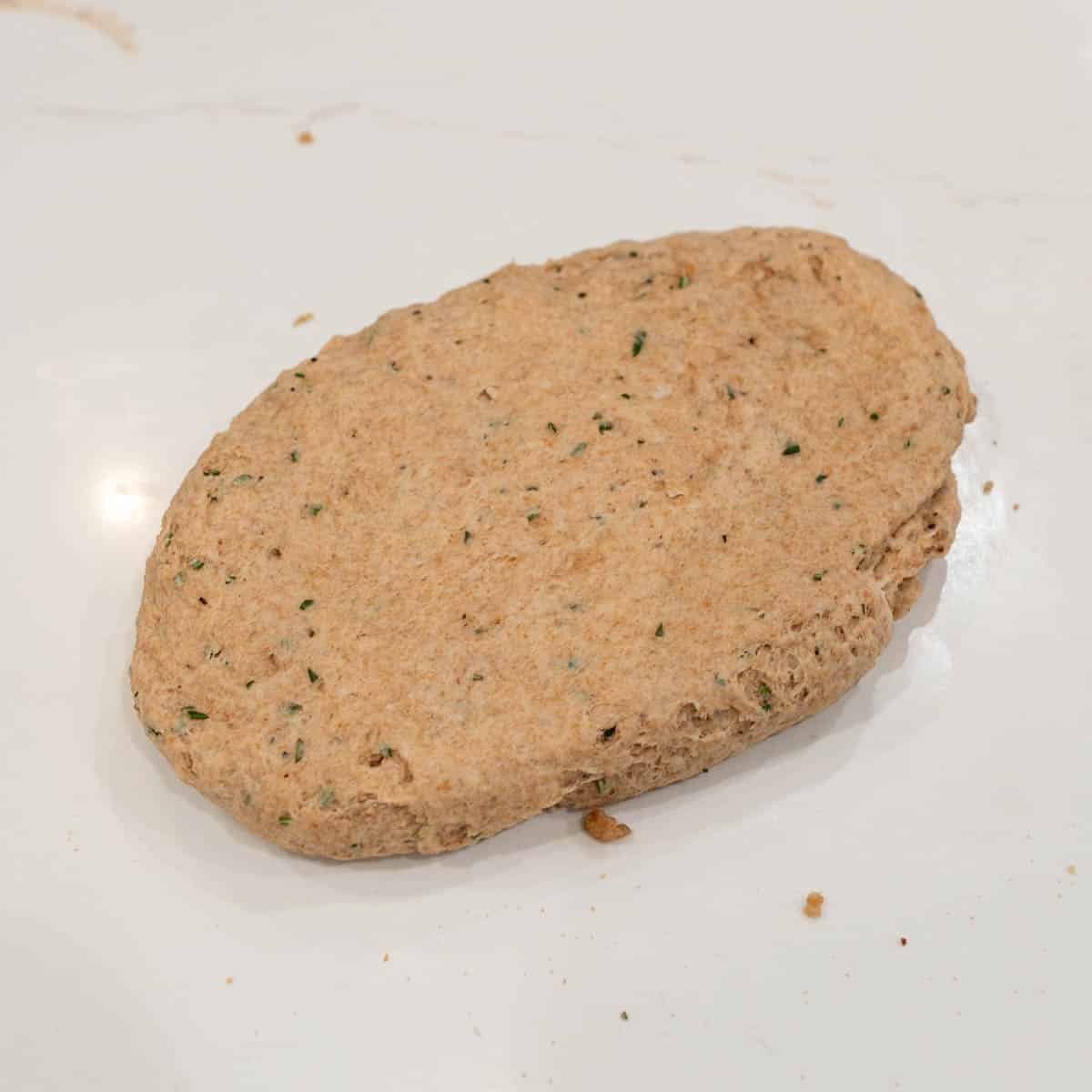 Sourdough discard cracker dough formed into a smooth, flattened ball on a marble countertop.
