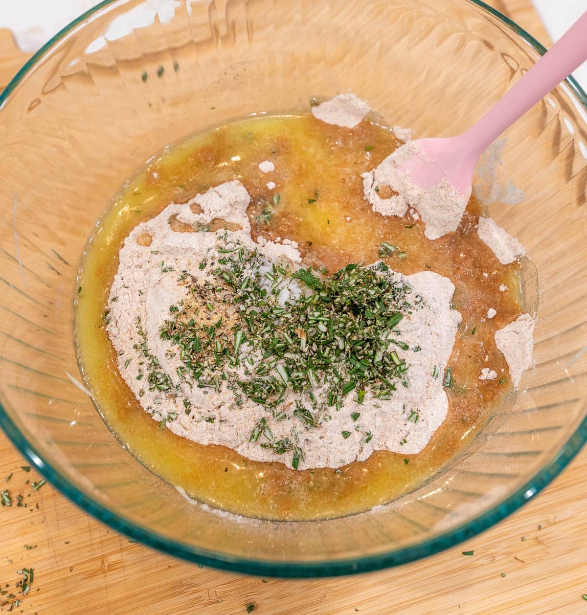 Sourdough starter, flour, melted butter, rosemary, and seasoning in a glass mixing bowl with a rubber spatula. 