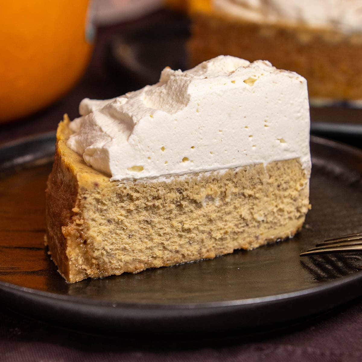 A slice of Pumpkin Cheesecake topped with homemade whipped cream.