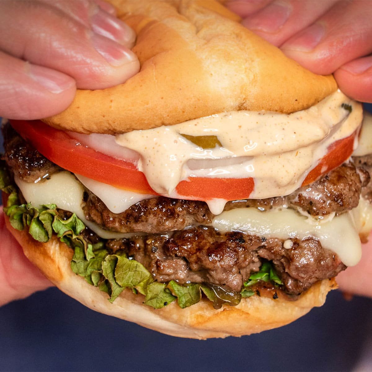 A close up photo of a juicy smash burger pressed down by two hands.