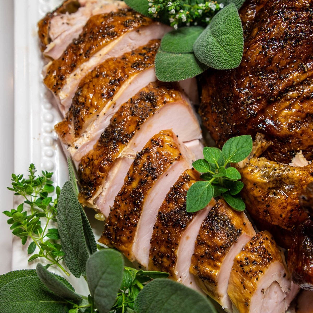 Slices of smoked turkey on a white platter and garnished with fresh herbs.