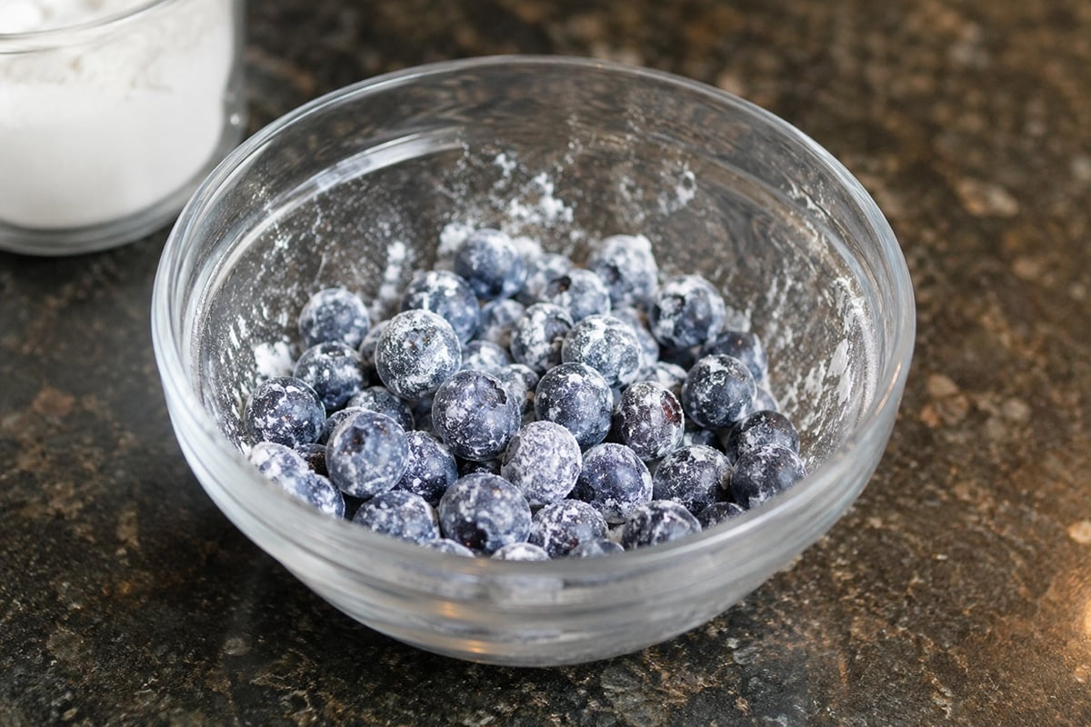 Close up of fresh blueberries dusted with flour in a clear glass bowl.