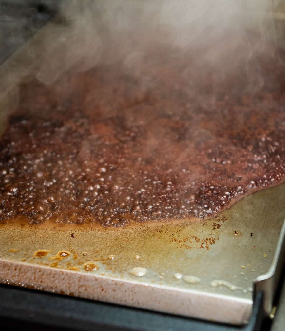 The flat-top griddle is bubbling while being deglazed.