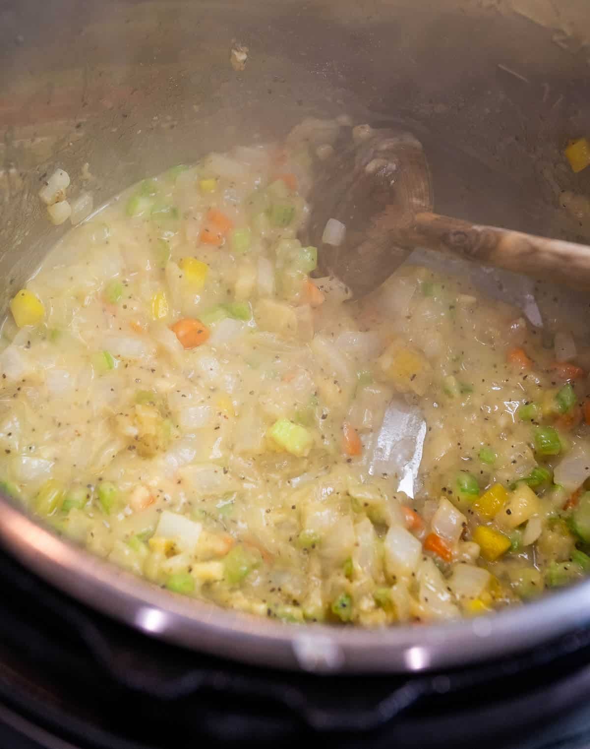 Flour is added to the vegetables, garlic, and butter, which is then stirred together with a wooden spoon.