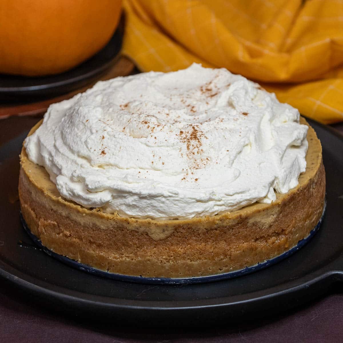 A whole pumpkin cheesecake topped with homemade whipped cream, and a sprinkle of pumpkin pie spice. 