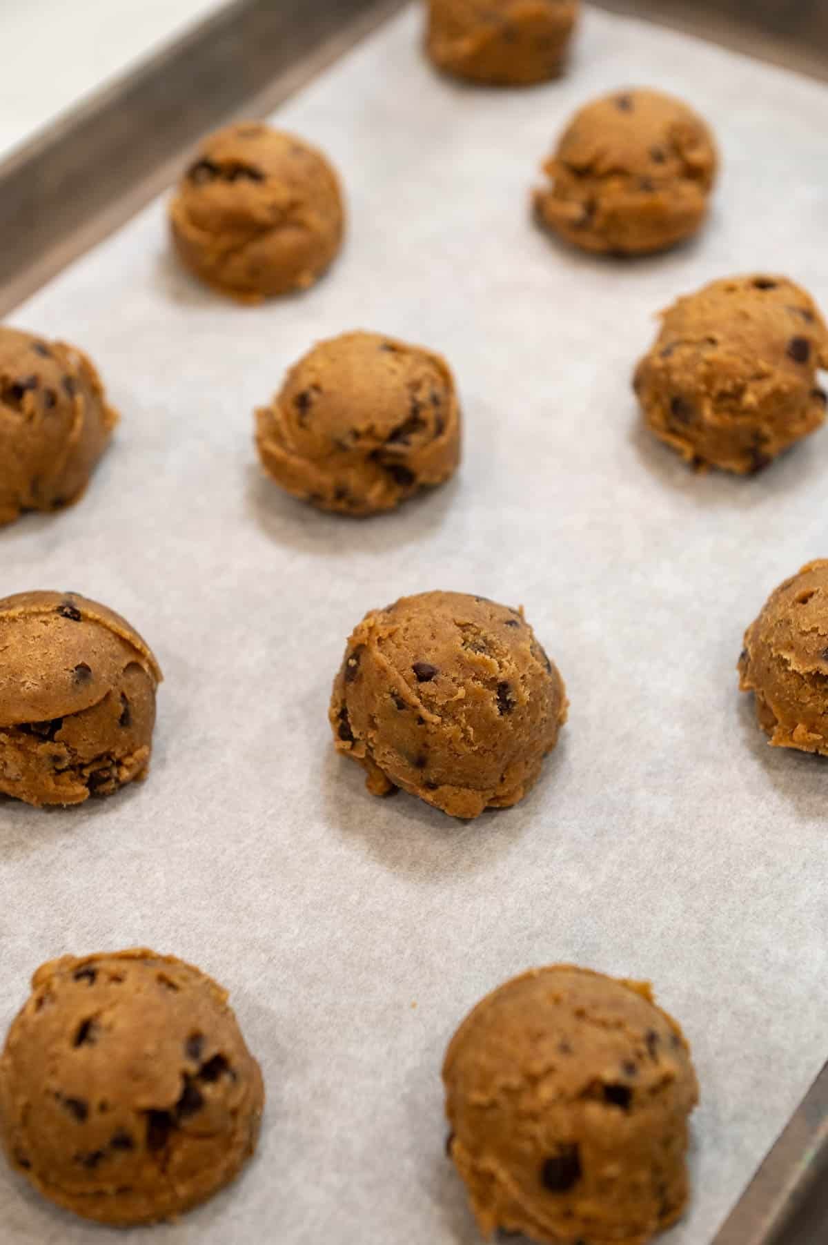 Scoops of pumpkin chocolate chip cookie dough on a lined baking sheet. 
