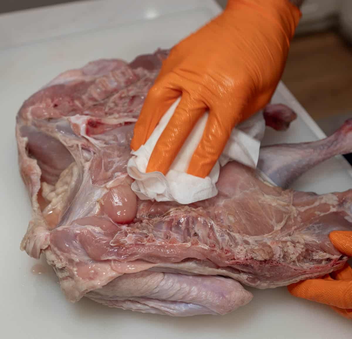 Raw turkey is being patted with a paper towel to dry. 