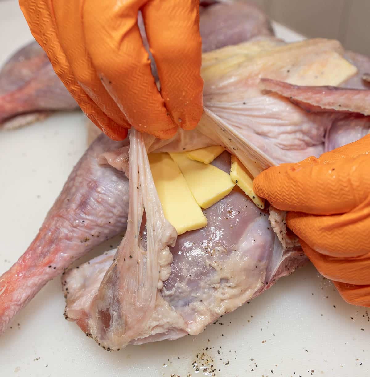 A gloved hand is lifting up the turkey skin, and butter has been inserted in side. 
