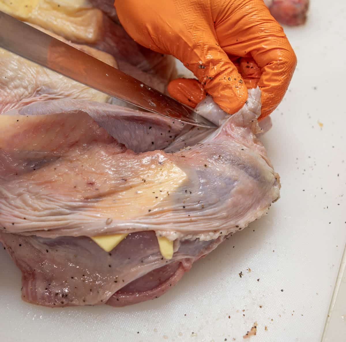 A gloved hand is cutting into the skin of the turkey to create a small pocket. 