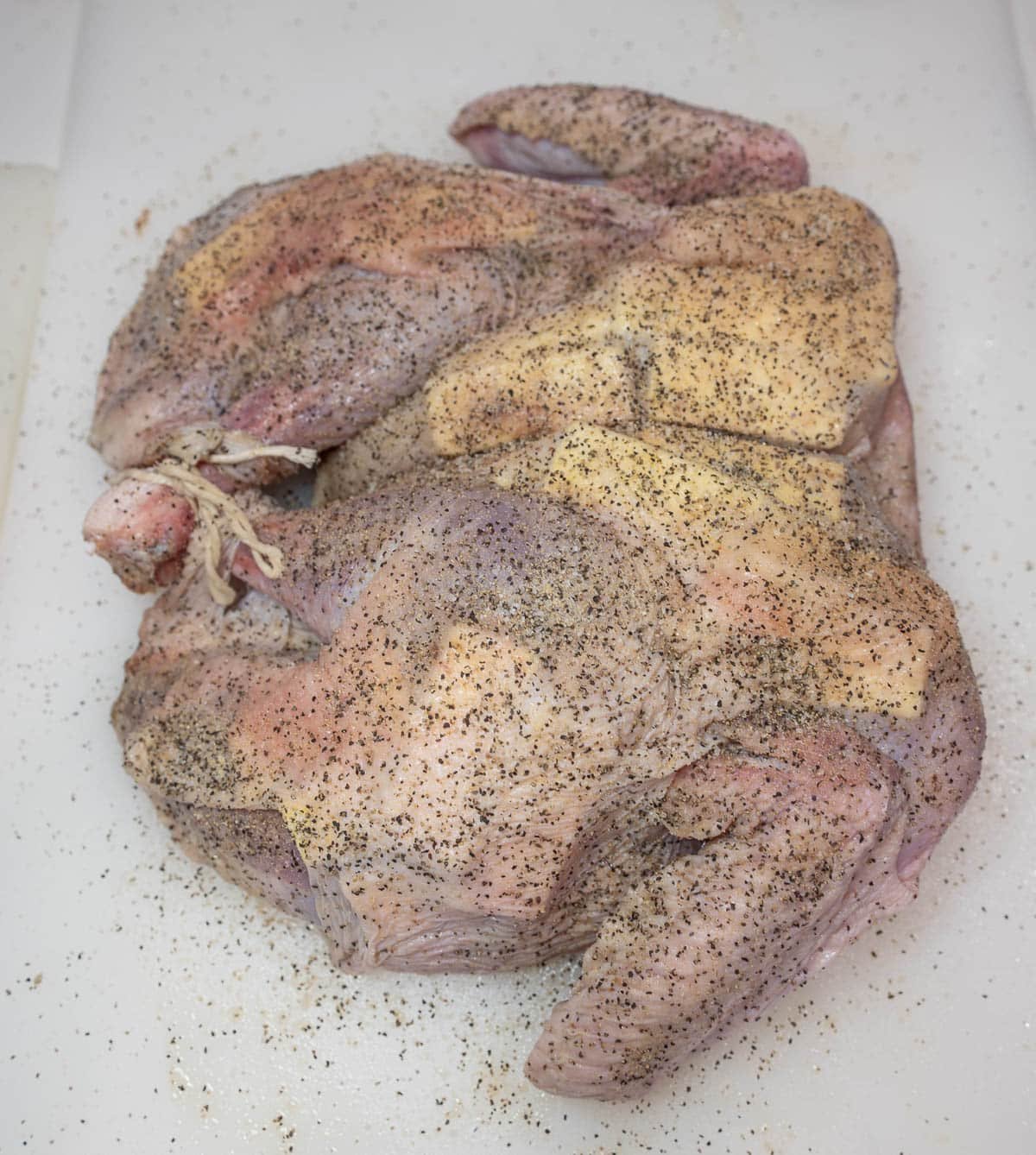 Raw, spatchcocked turkey tied, seasoned, and pull of butter.