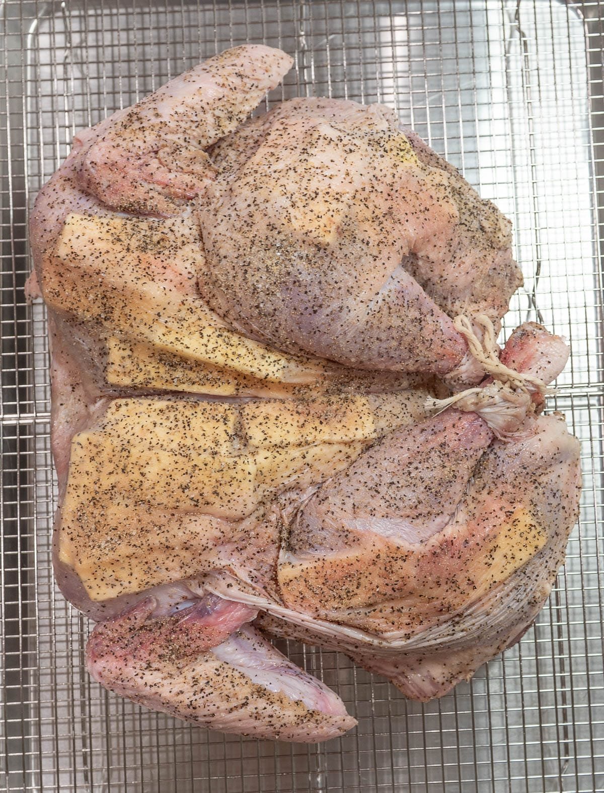 The raw, prepped turkey is on a stainless steal rack. 