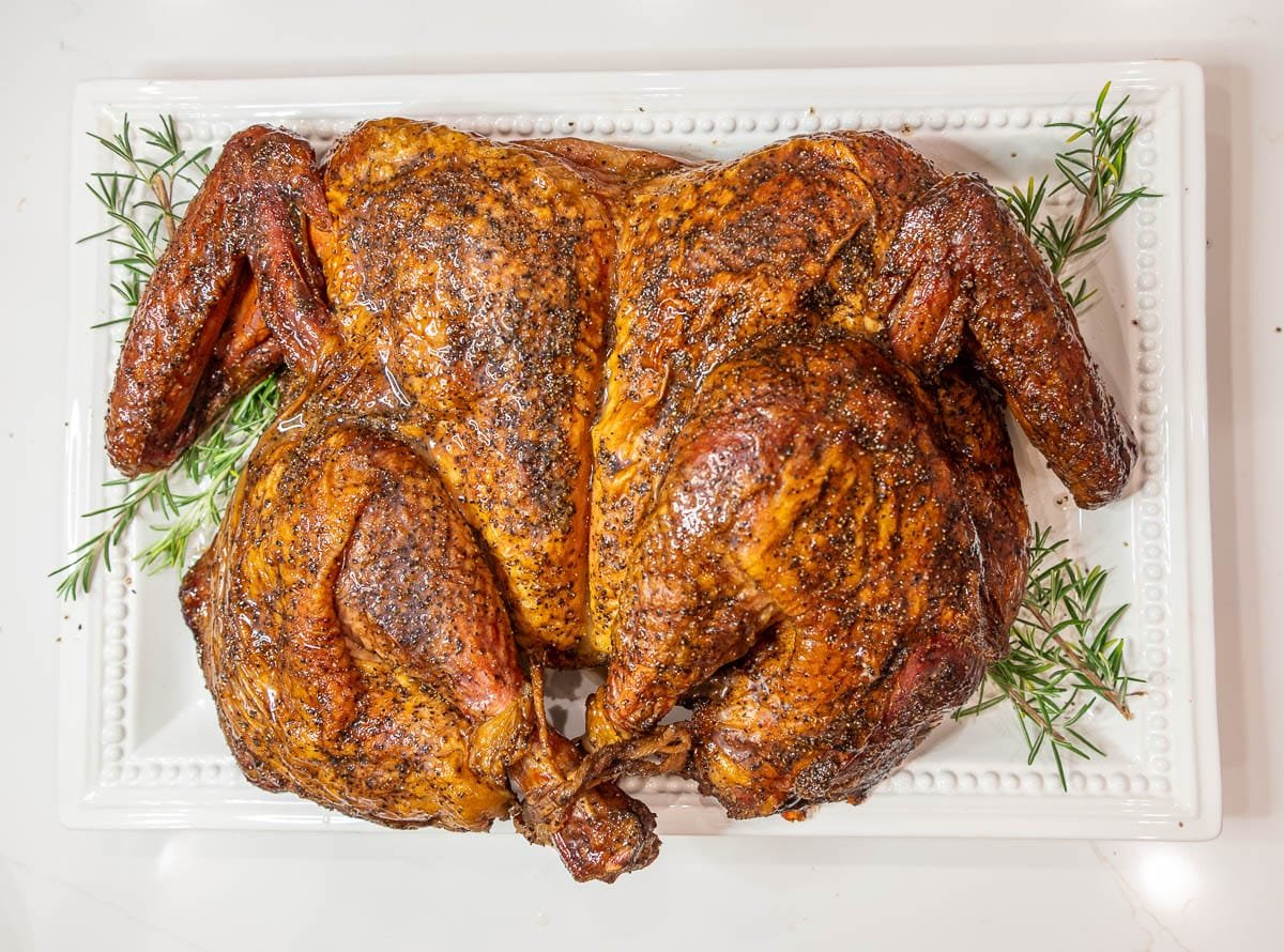 The finished Smoked Turkey on a white platter with fresh rosemary as a garnish. 