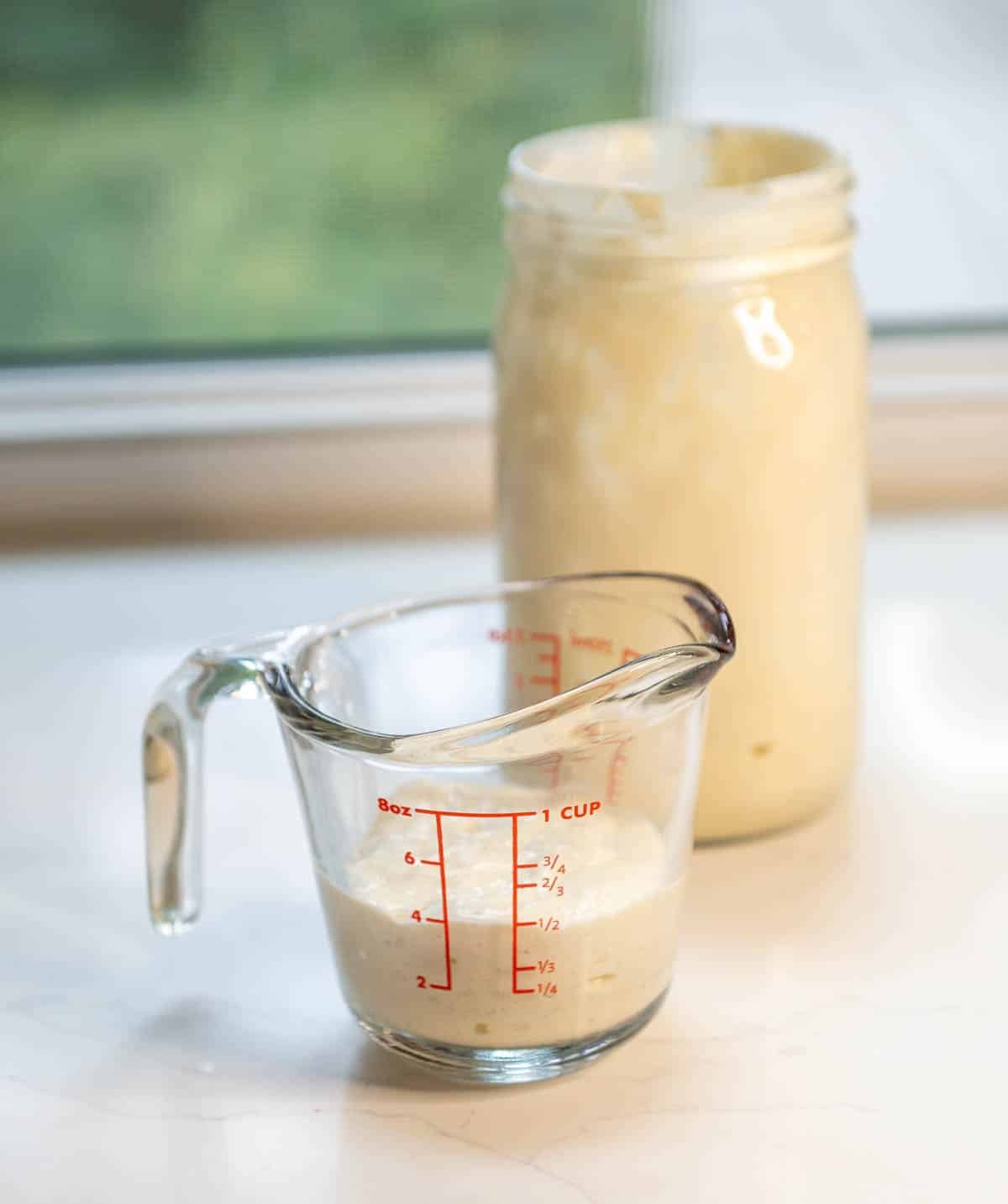 A glass liquid measuring cup filled with sourdough starter discard. 