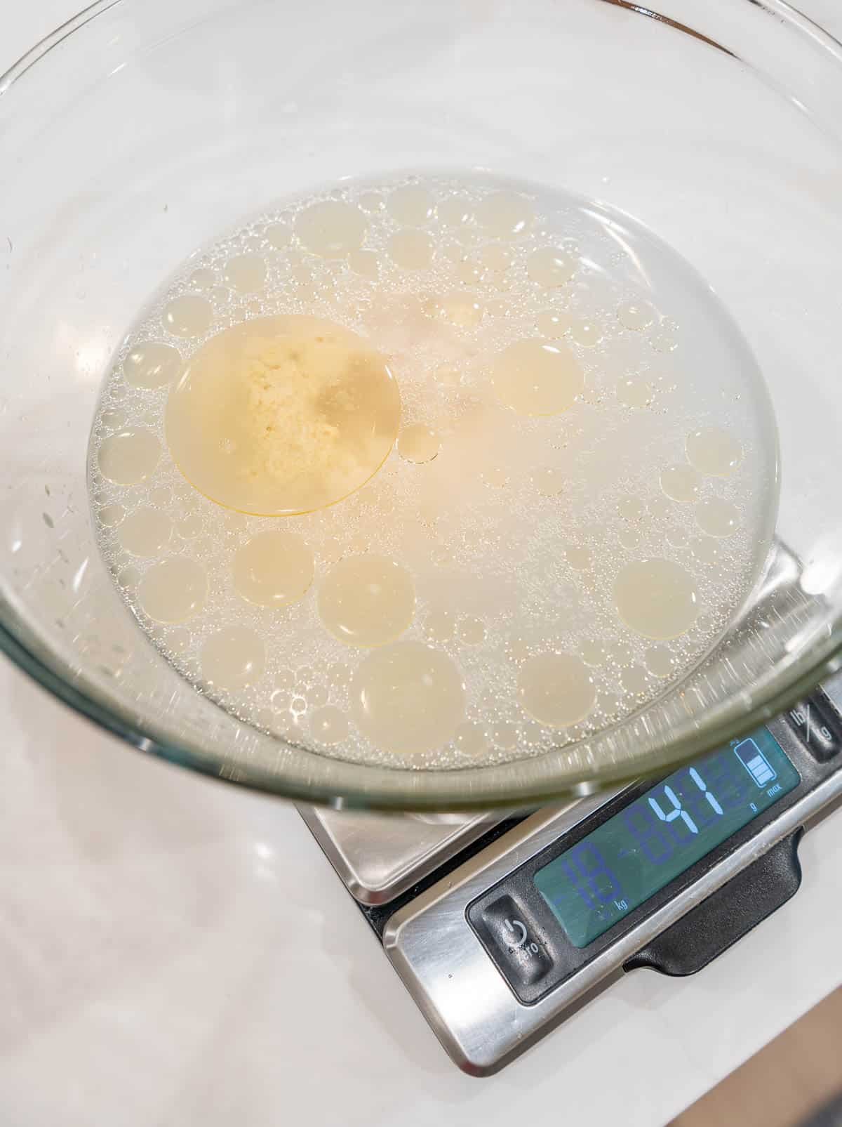 Sourdough starter, warm water, avocado oil, and honey in a bowl, sitting on a food scale. 