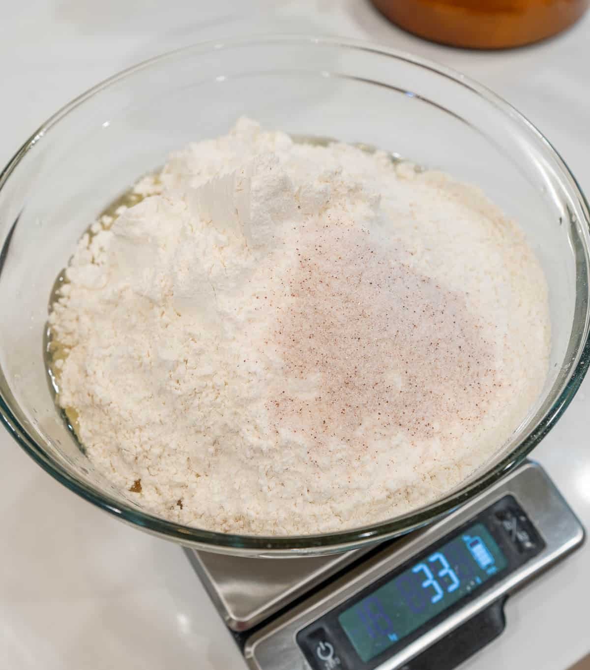 Dry ingredients added to the wet ingredients, in a bowl, sitting on a food scale. 