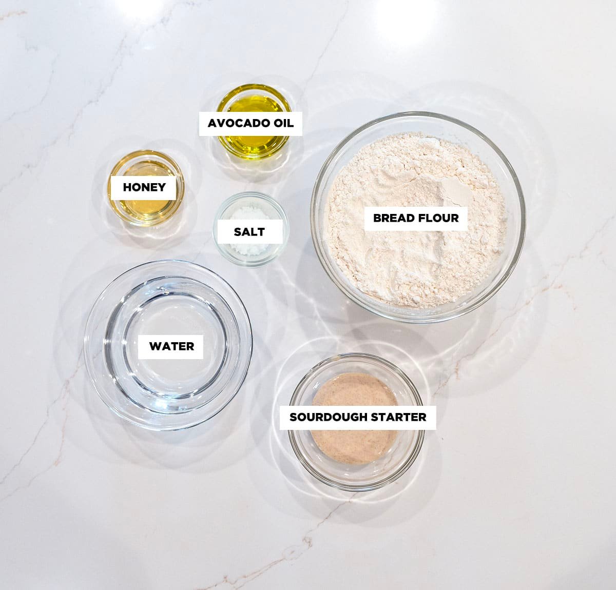 Ingredient shot for Sourdough Rolls, featuring: bread flour, water, sourdough starter, avocado oil, honey, and salt. 